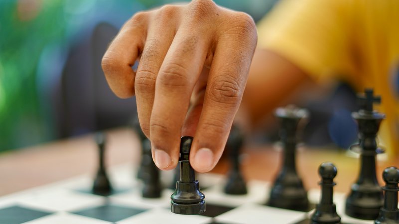 Hand mit schwarzem Bauern über Schachbrett