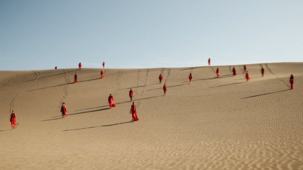 Frauen in roten Gewändern auf einer Düne