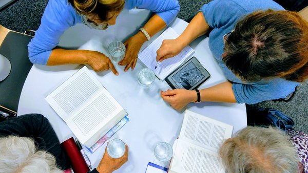 Personen mit aufgeschlagenen Büchern und eReader um einen Tisch