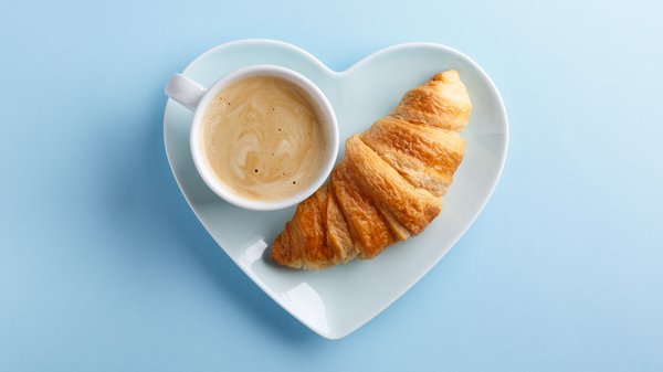 Eine Tasse Kaffee und ein Croissant auf einem herzförmigen Teller