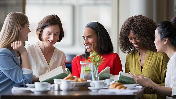 eine Gruppe Frauen mit Büchern unterhält sich an einem Tisch