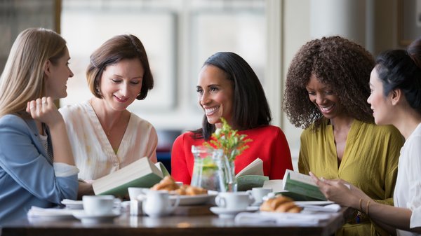 eine Gruppe Frauen mit Büchern unterhält sich an einem Tisch